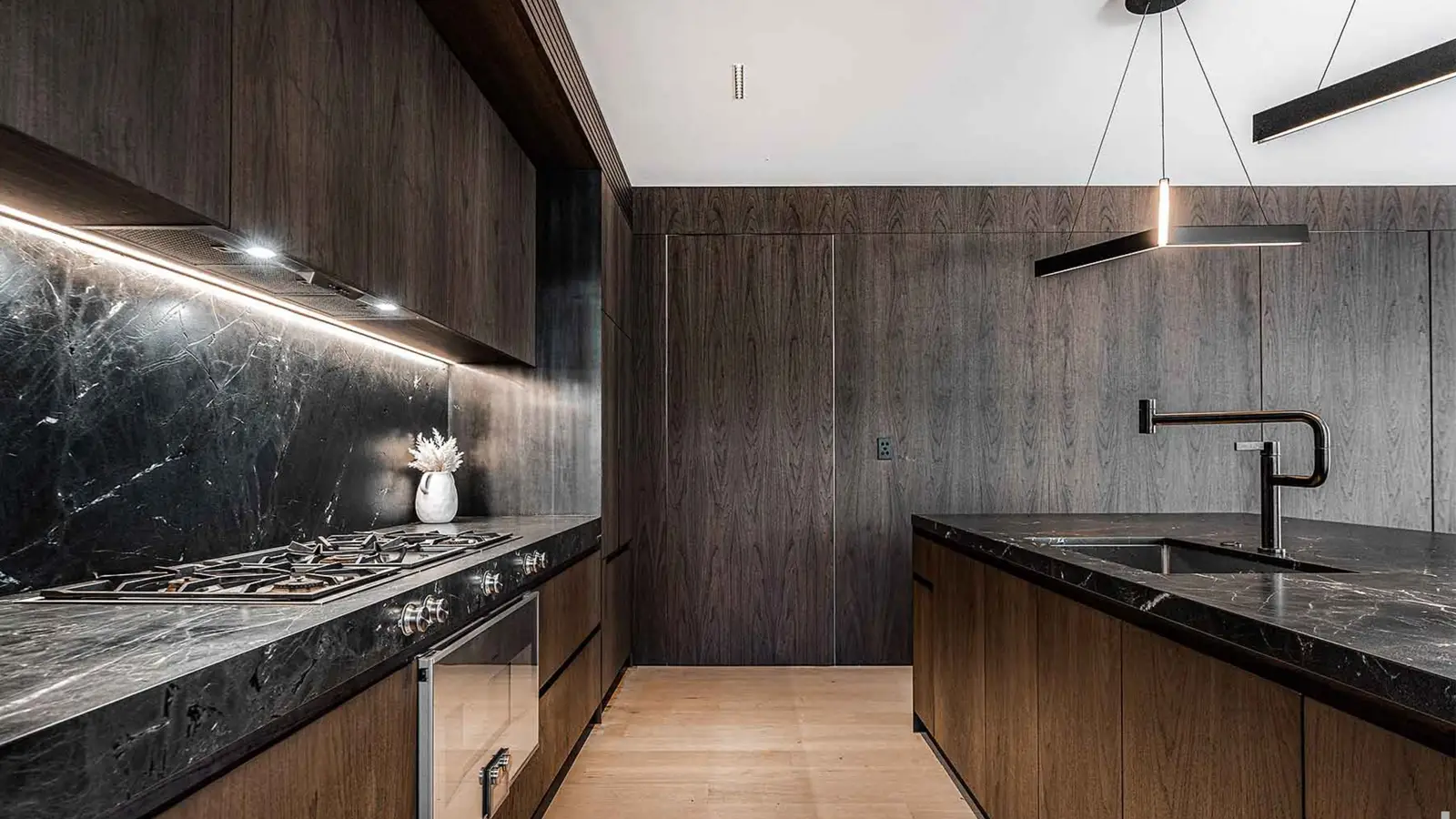 Modern dark-toned kitchen by DBJ Furniture, featuring a waterfall-edge stone island, black tapware, and seamless veneer cabinetry.